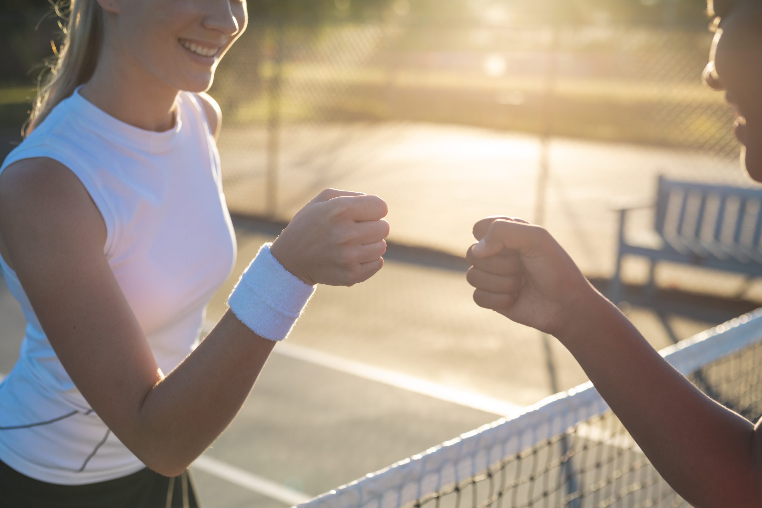 Smiling multiracial young female tennis players giving fist bump over net at court