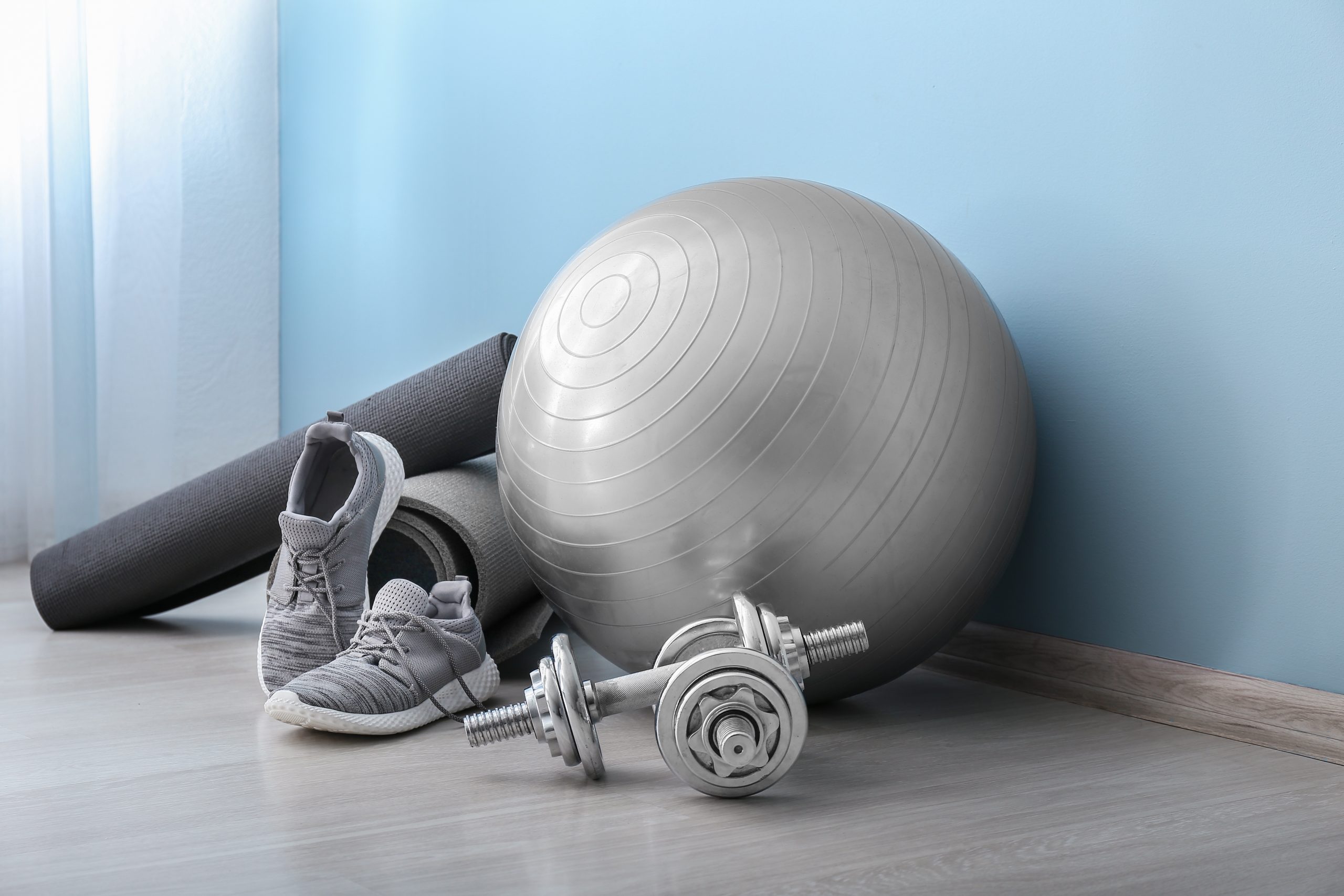 Set of sports equipment with fitness ball and shoes near color wall