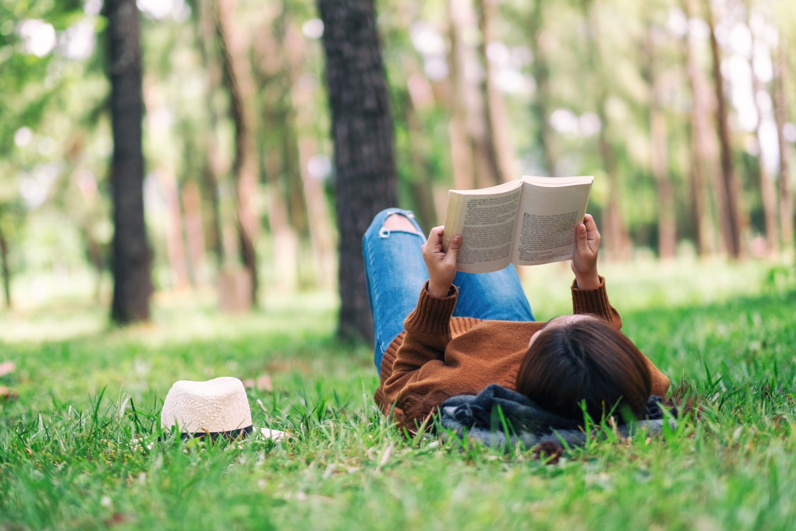 A beautiful Asian woman lying and reading a book in the park